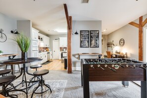 A modern kitchen with white cabinets, a dining area with a foosball table, and a large plant.