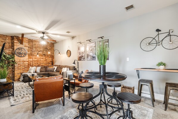 A cozy living room with a brick wall, a ceiling fan, a round coffee table, and a bicycle mounted on the wall.