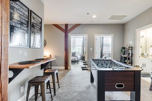 A spacious room with a foosball table, wooden bar counter, and a large window.