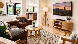 Ein Wohnzimmer mit Sofa, Couchtisch und Fernseher, im Hintergrund eine Küche und eine Wüstenlandschaft an der Wand.