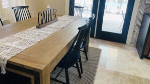 Ein Essbereich mit einem Holztisch, schwarzen Stühlen, einer Makramee-Tischläufer und einem Schild mit der Aufschrift 'GATHER'.