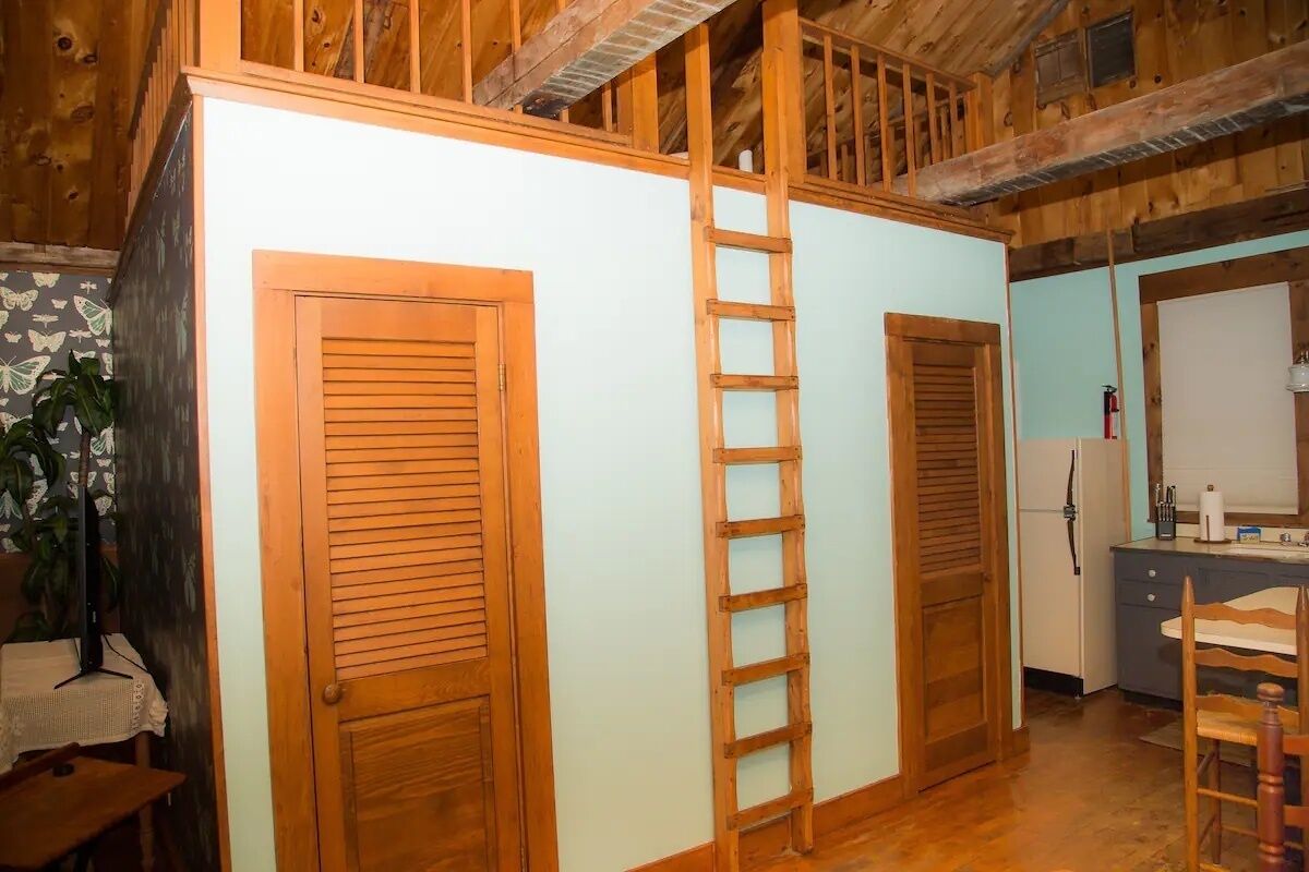 A room with wooden doors, a ladder, a kitchen area, and a dining table.