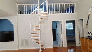Una habitación con una escalera blanca, un televisor y una puerta que da a otra estancia.