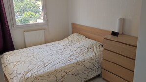 Een slaapkamer met een bed, een dressoir, een radiator en een raam met uitzicht op groen.