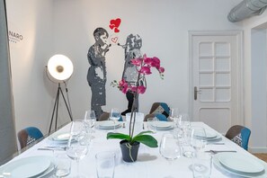 A dining area with a table set for four, a potted orchid, and a wall art depicting two figures with hearts.