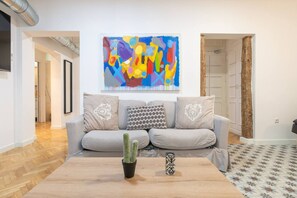 A living room with a grey sofa, a colorful abstract painting, and a cactus on a wooden coffee table.