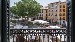 A balcony with a view of a square with outdoor seating, trees, and buildings with balconies. - Exclusive BANKSY DOWNTOWN, by MONARO***** (Madrid)