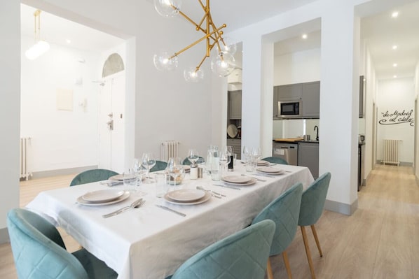 Un espace repas avec une longue table dressée pour un repas, des chaises et un lustre moderne.