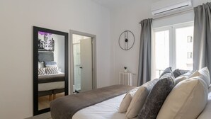 A bedroom with a bed, a mirror, a radiator, and a window with curtains. - Exclusive BANKSY DOWNTOWN, by MONARO***** (Madrid)