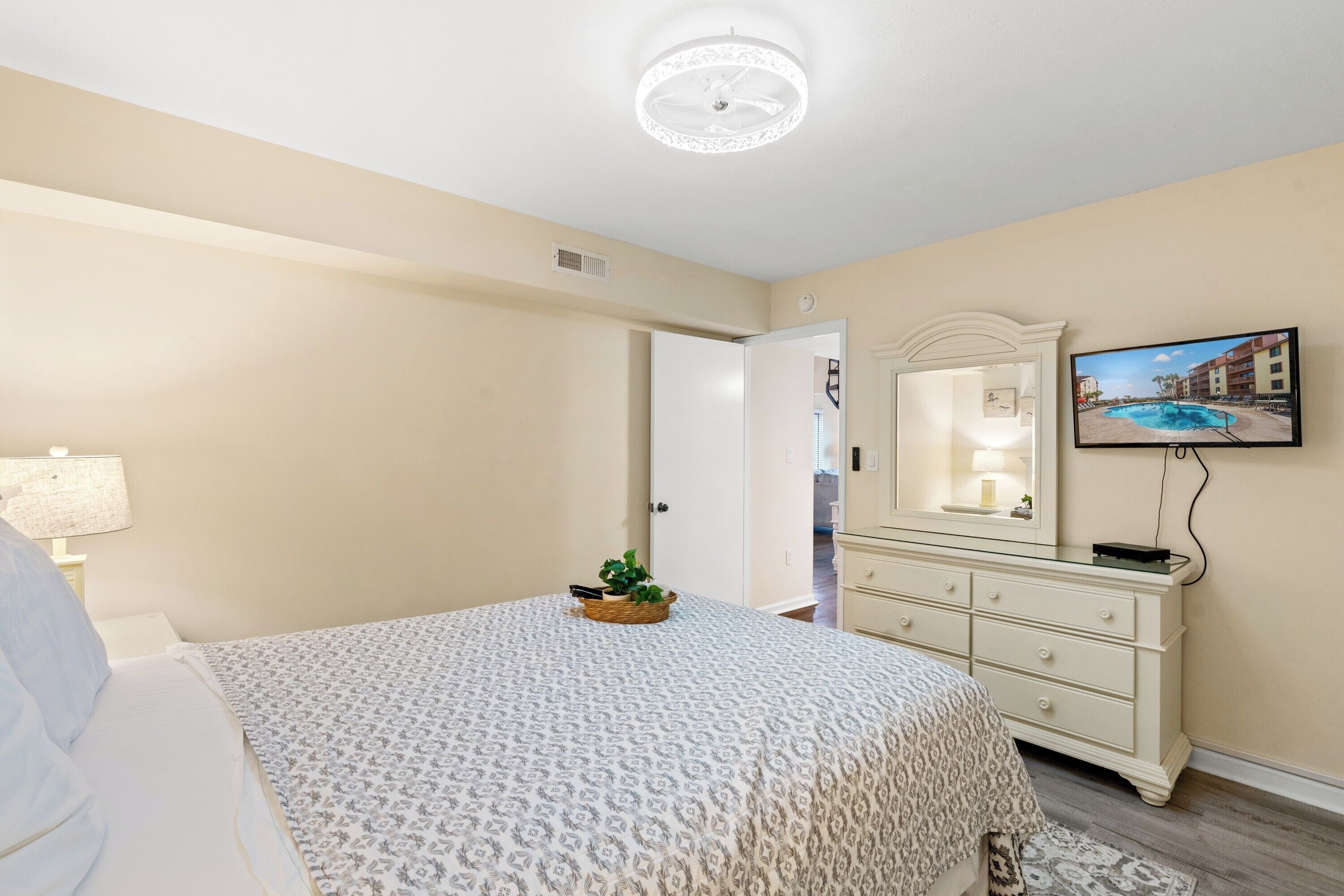 A bedroom with a bed, a dresser, a television, and a door leading to another room.