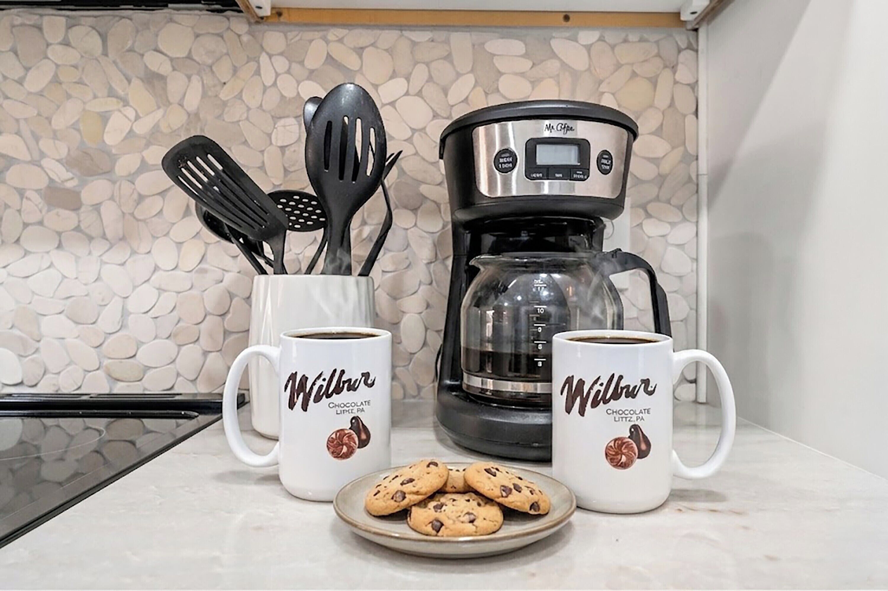 Eine Küche mit zwei Kaffeetassen, einem Teller Kekse und einer Kaffeemaschine.