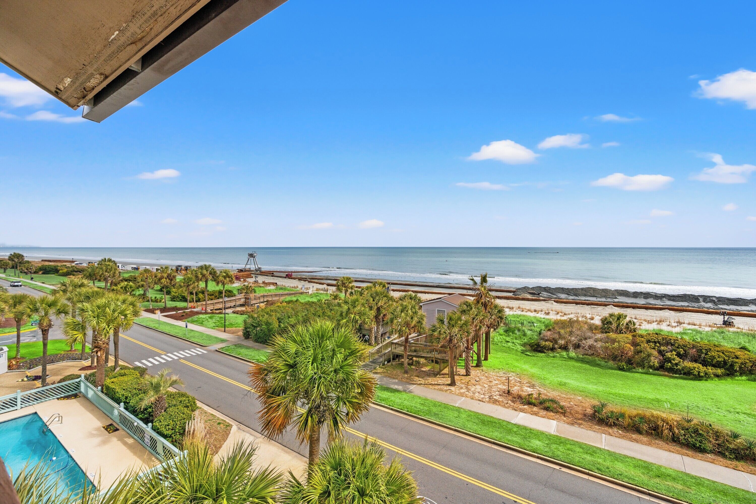 A residential area with a pool, palm trees, and a view of the ocean.
