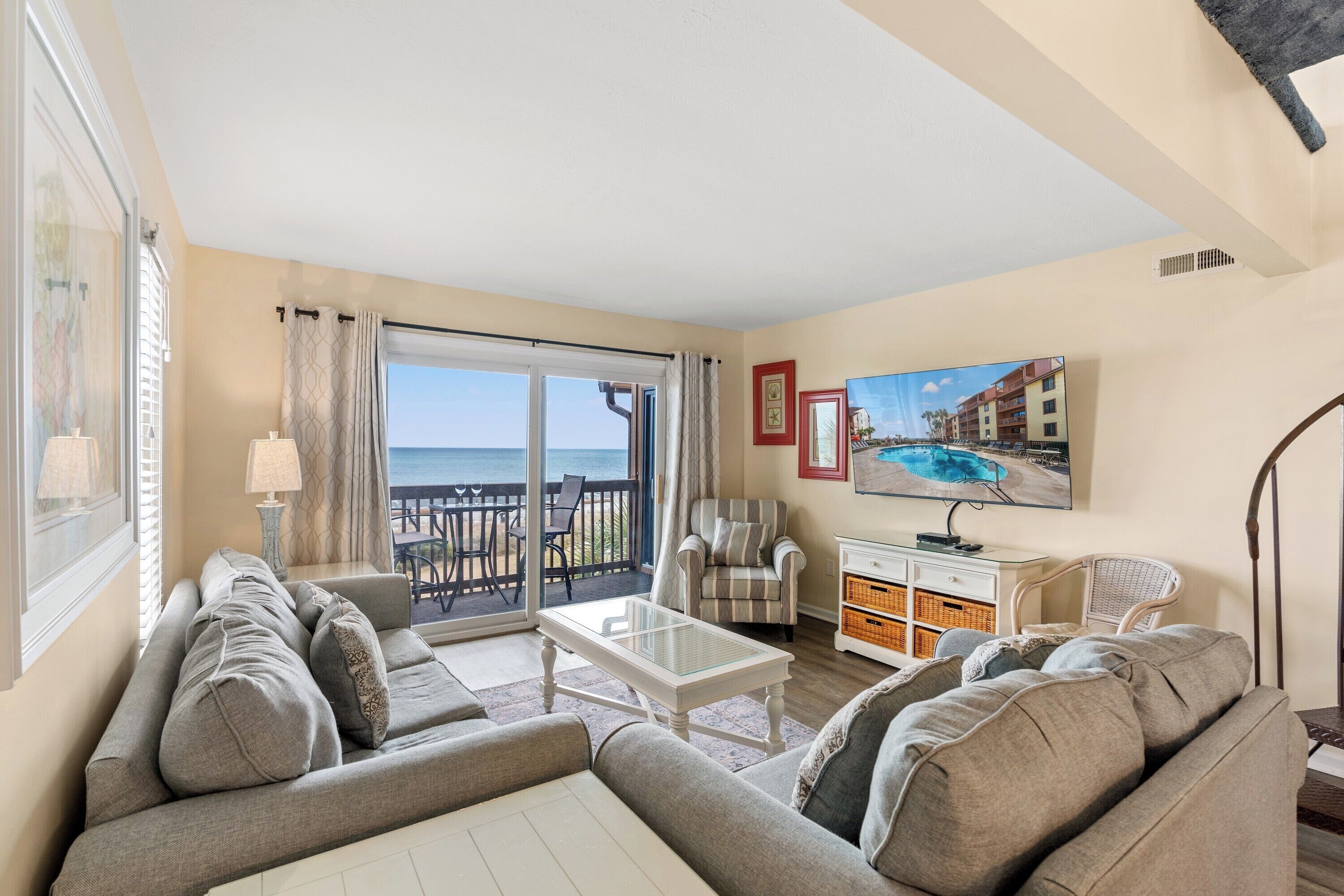 Un salon comprenant un canapé, des fauteuils, une table basse et un téléviseur. Il y a un balcon avec vue sur la mer.