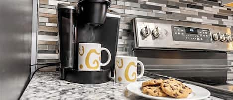 A kitchen with a coffee maker, two coffee cups, and a plate of cookies.