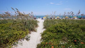 A sandy beach path with beach umbrellas and people in the distance. - Anchorage I & II by Elliott Beach Rental (Myrtle Beach)