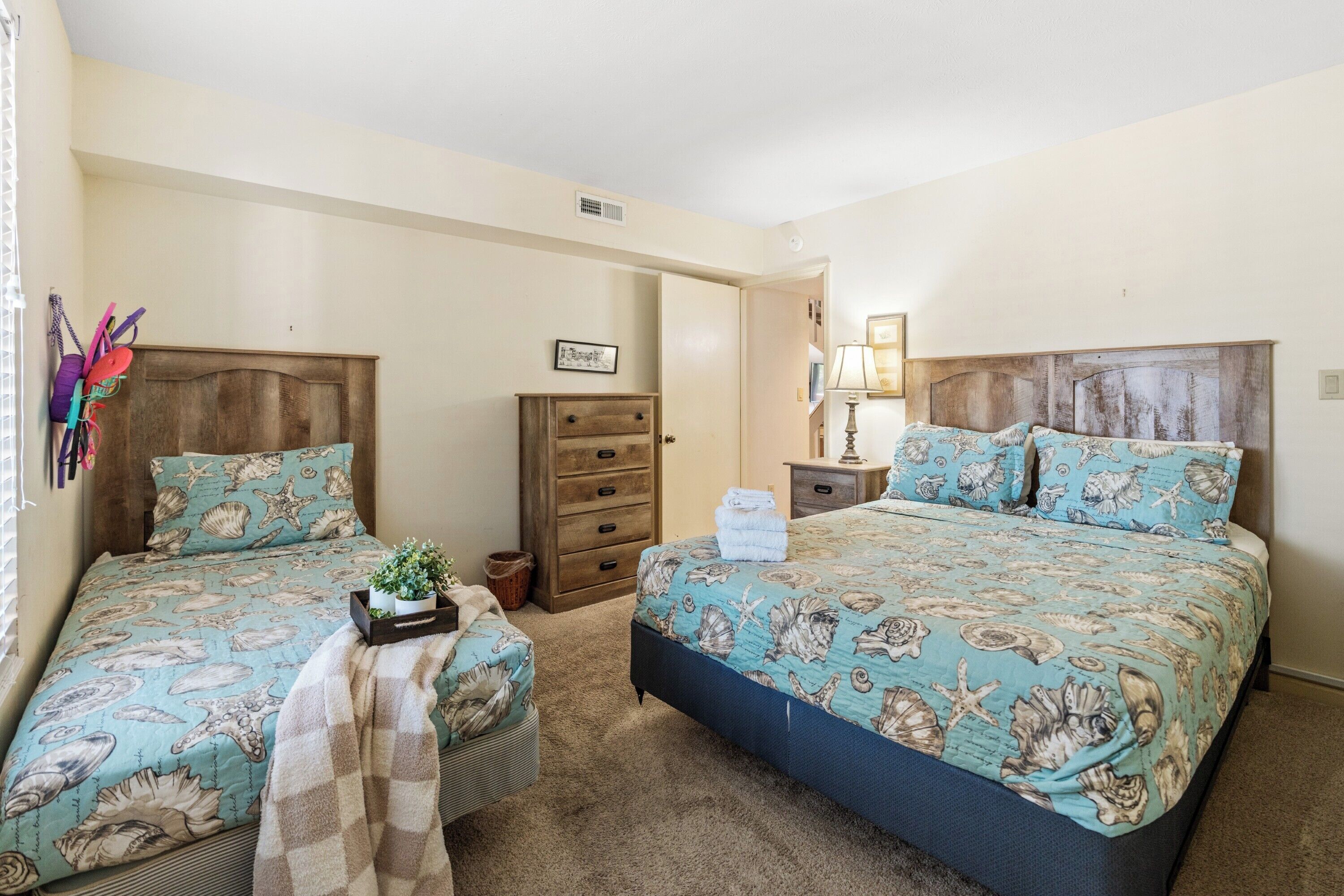 A bedroom with two beds, a dresser, a nightstand, a lamp, and a small table with a plant.