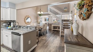A spacious kitchen with a central island, a dining area with chairs, a staircase, and a living room with a sofa. - Anchorage I & II by Elliott Beach Rental (Myrtle Beach)