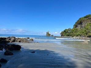 A beach with clear blue water, rocky outcrops, and dense greenery. - House,Pool in the jungle.Great location short walk to famous Playa la Macha (Quepos)