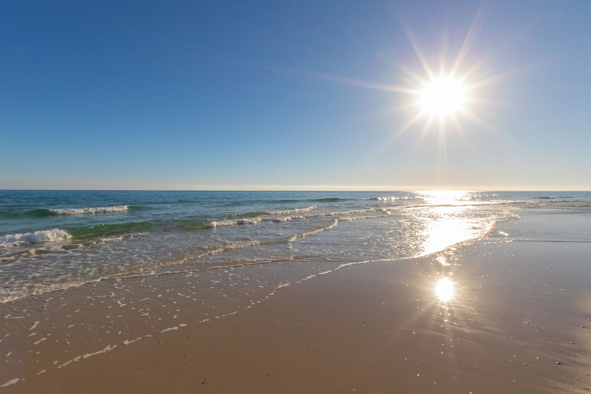 A beach with waves and a bright sun.