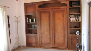 Una habitación con un armario de madera grande, una estantería y un perchero.