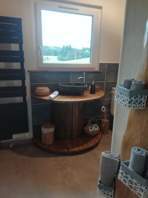 Een moderne badkamer met een ronde houten wastafel, een zwarte wasbak en een raam met uitzicht op bomen.