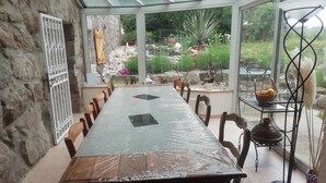 Un invernadero con una larga mesa de comedor, sillas y techo de cristal.