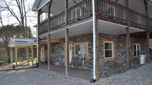 A two-story stone building with a covered patio area, outdoor seating, and a wooden deck.