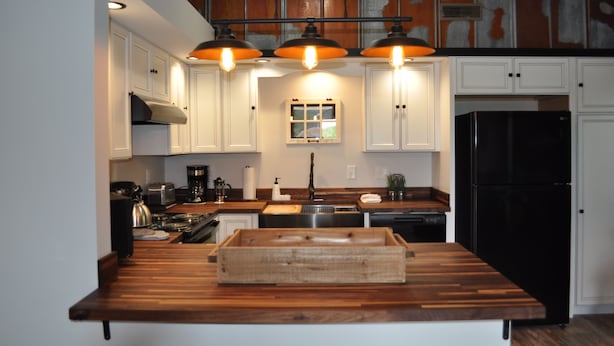 A kitchen with white cabinets, a black refrigerator, and a wooden countertop.