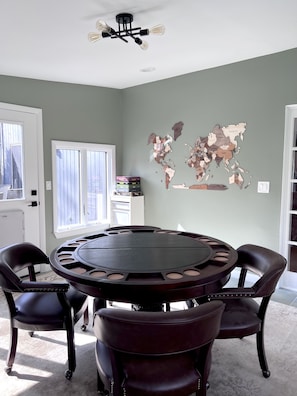 A dining area with a round table, four chairs, a world map on the wall, and a ceiling fan.