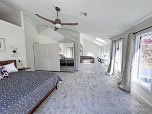 A spacious bedroom with a large bed, a ceiling fan, a wardrobe, and a dining area with chairs.