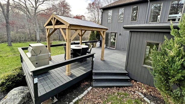 En overdækket udendørs terrasse med grill, spisebord og stole.