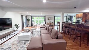 En rummelig opholdsstue med stor sofa, fladskærm og spiseplads med barstole.