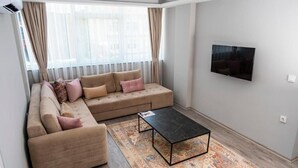A modern living room with a beige sectional sofa, a black coffee table, and a patterned rug. - Comfort Center (Edirne)