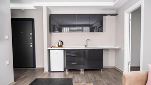 A compact kitchen with dark cabinets, a white countertop, and a small refrigerator. - Comfort Center (Edirne)