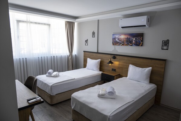 A hotel room with two beds, a desk, a chair, an air conditioner, and a cityscape painting on the wall. - Comfort Center (Edirne)