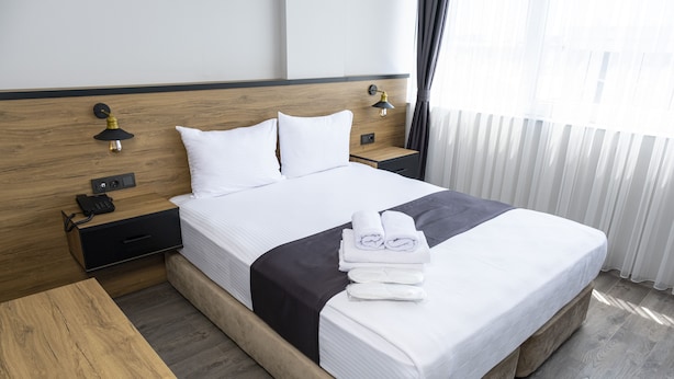 A hotel room with a large bed, two bedside tables, a wooden nightstand, and a window with curtains. - Comfort Center (Edirne)