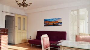 Ein Zimmer mit einer roten Couch, einem Glastisch und einem Gemälde eines Gebäudes an der Wand.