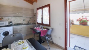 A compact kitchen with a dining area, a washing machine, and a view of a yellow building through a window. - 2 bedroom amazing apartment in Riola Sardo (Riola Sardo)