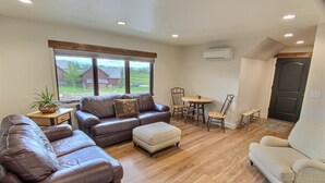 A spacious living room with leather sofas, a wooden dining table, and a view of a rural landscape through large windows.