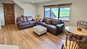 A spacious living area with two leather sofas, a wooden dining table, and a view of the outdoors.