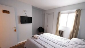 A hotel room with a bed, a television mounted on the wall, a door with a number, and a window with curtains. - Hotel Provincia (Trelew)