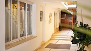 A hallway with a staircase leading to a wooden staircase, a potted plant, and a door with a sign. - Hotel Provincia (Trelew)