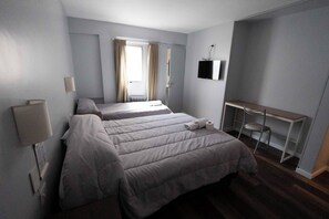 A hotel room with two beds, a desk, a chair, a TV, and a window with curtains. - Hotel Provincia (Trelew)