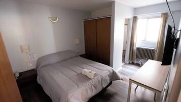 Ein Schlafzimmer mit Bett, Schreibtisch, Kleiderschrank und einem Fenster mit Vorhängen.