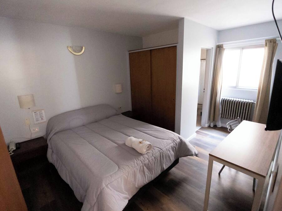 Ein Schlafzimmer mit Bett, Schreibtisch, Kleiderschrank und einem Fenster mit Vorhängen.