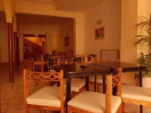 A dining area with wooden chairs and a black table, a staircase in the background, and a potted plant on the right. - Hotel Provincia (Trelew)