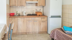 A compact kitchen with wooden cabinets, a kettle, a toaster, and a small refrigerator.