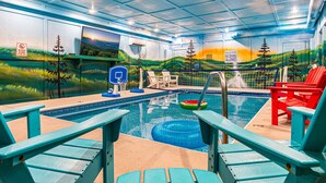 An indoor swimming pool with a basketball hoop, lounge chairs, and a mural of a landscape.