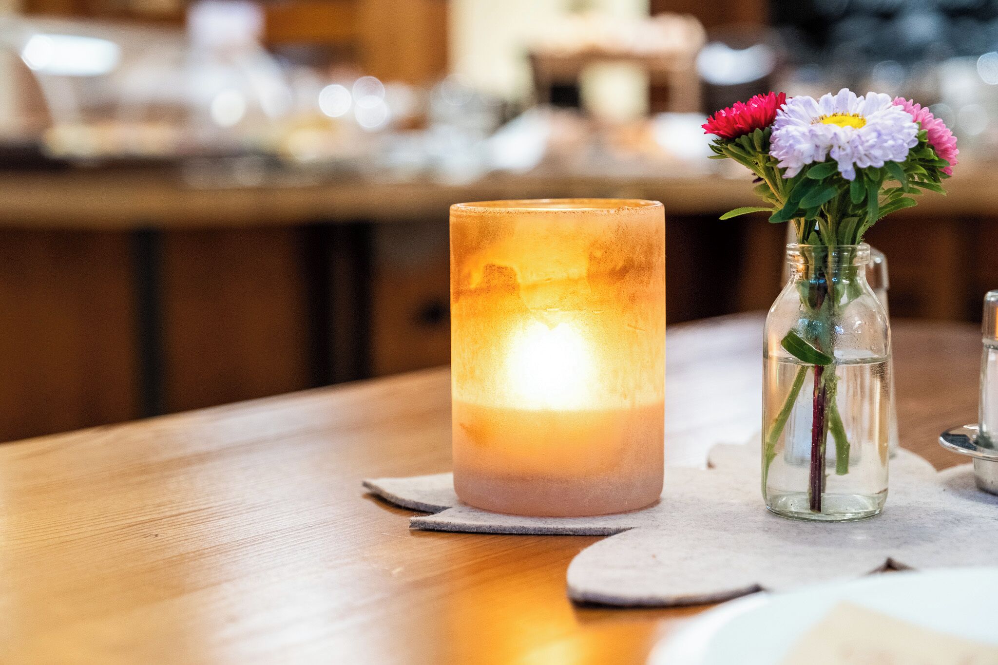 Ein Kerzenlicht mit Blumen in einem Glas auf einem Holztisch.