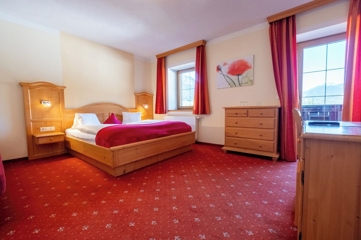 A bedroom with a wooden bed, a nightstand, a dresser, and a window with red curtains.